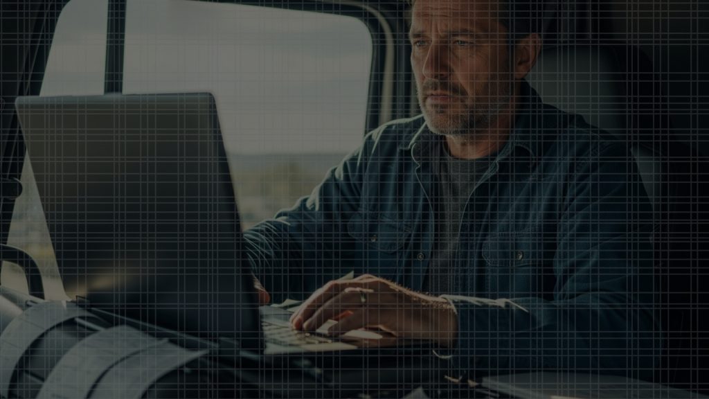 Independent truck driver reviewing load board on a laptop in a truck cab
